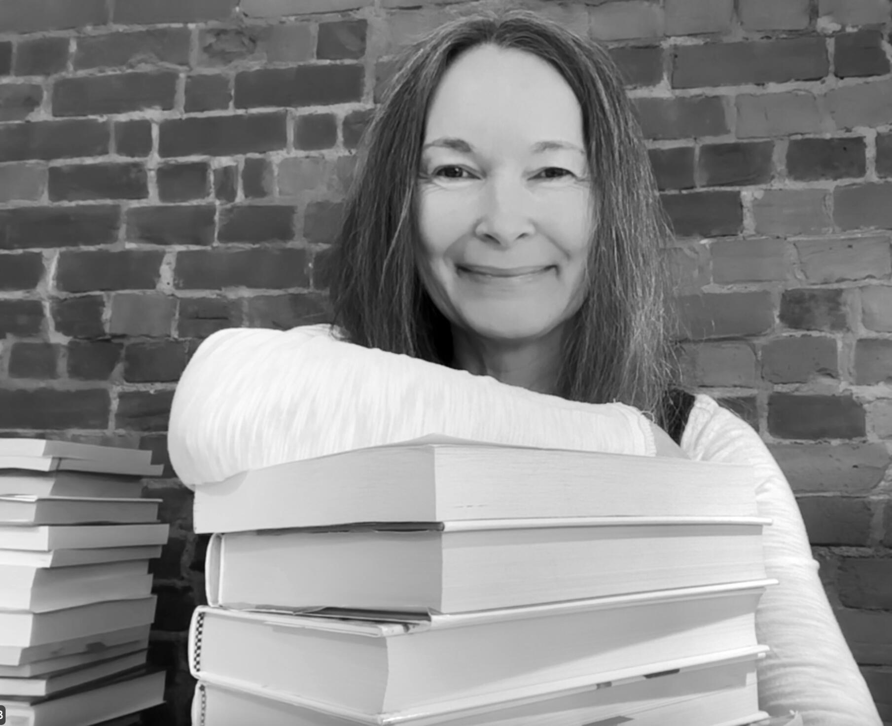 A photo of Michelle with a pile of books.